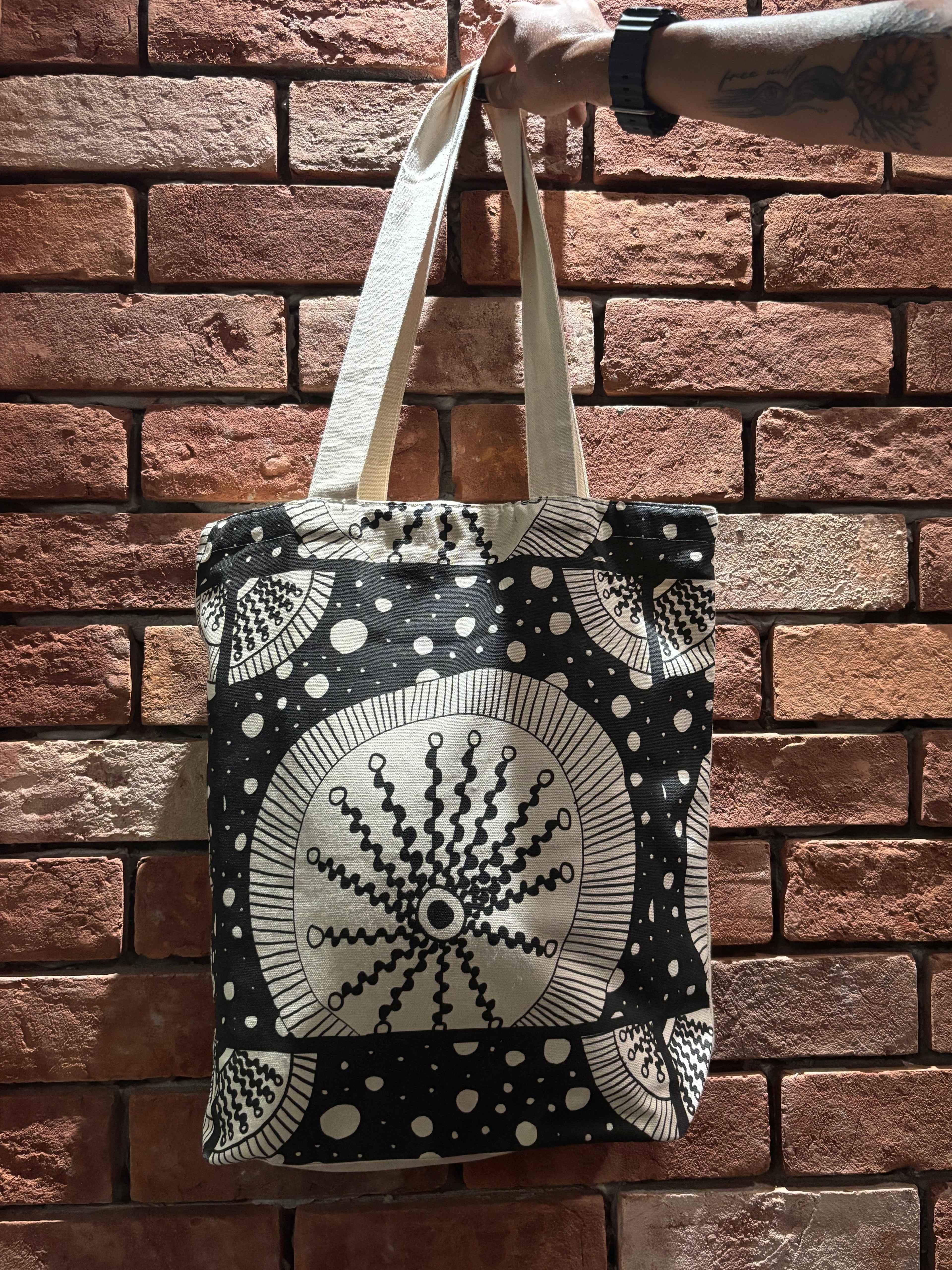 Tote bag with black and white pattern held against a brick wall